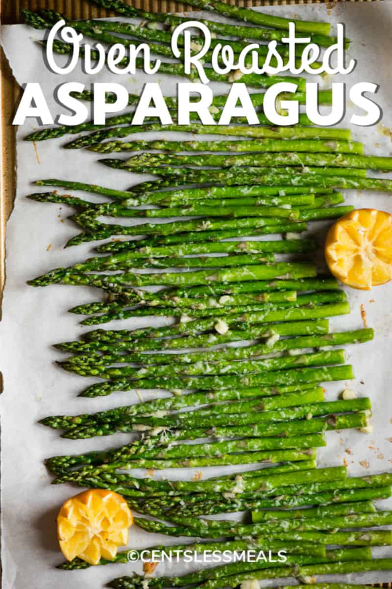 Oven Roasted Asparagus spread out on parchment paper garnished with oranges with a title