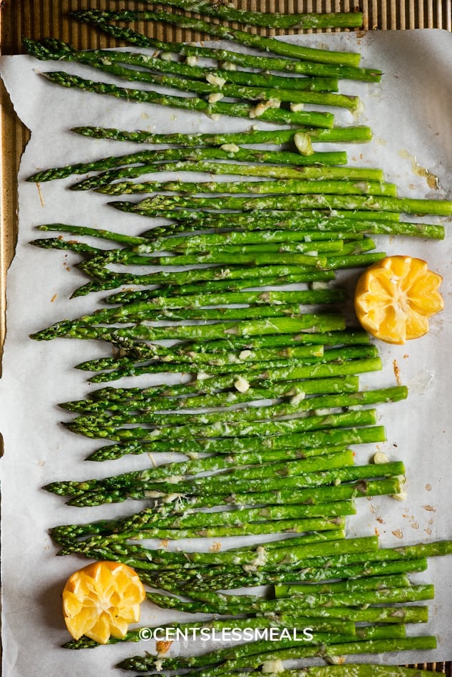 Oven Roasted Asparagus spread out on parchment paper garnished with oranges