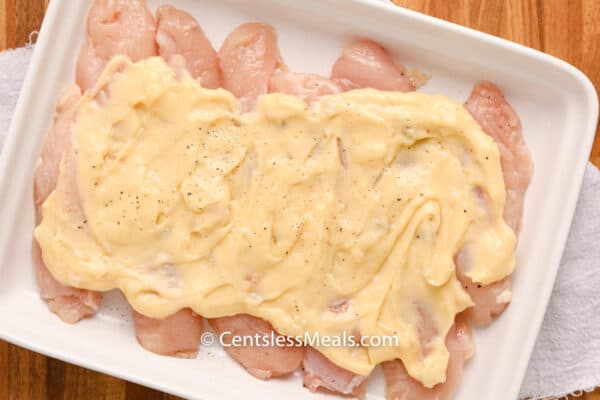 Raw chicken and sauce in a white casserole dish