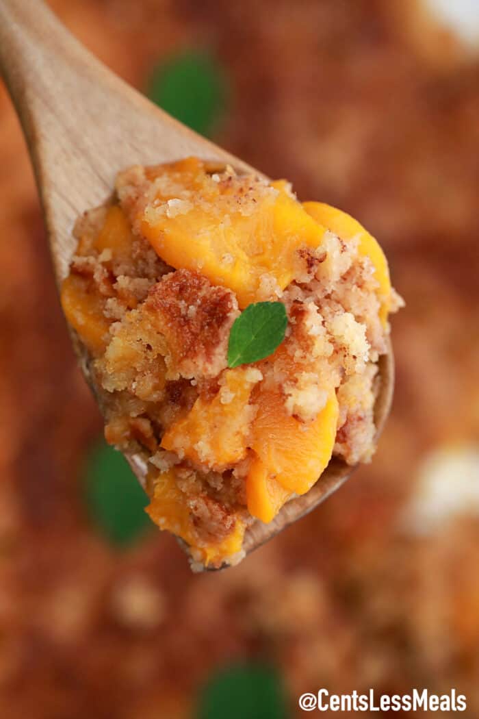 Peach Dump Cake on a wooden spoon with mint leaves.