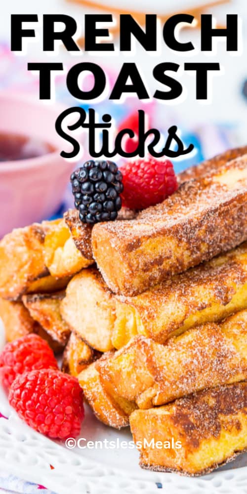 French toast sticks on a white plate with berries and a pink bowl of maple syrup in the background with a title