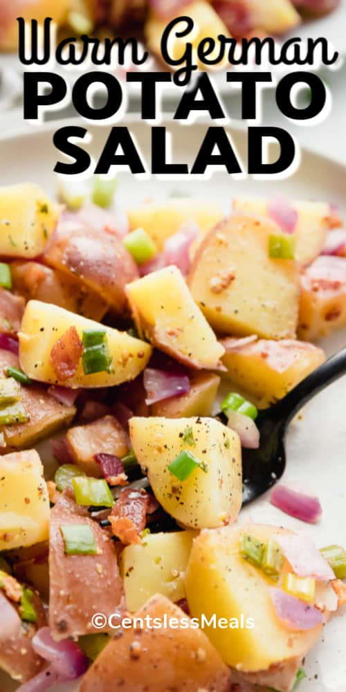 Warm German Potato Salad in a white bowl with a black fork, with writing.