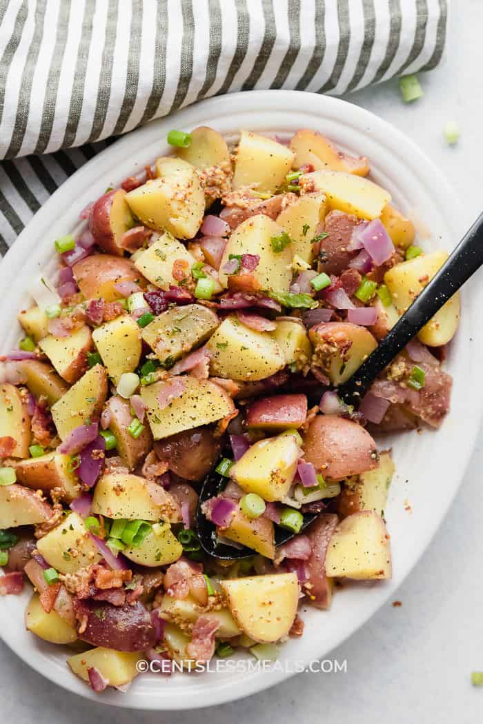 Warm German Potato Salad served on a white plate with black serving spoon on a light background