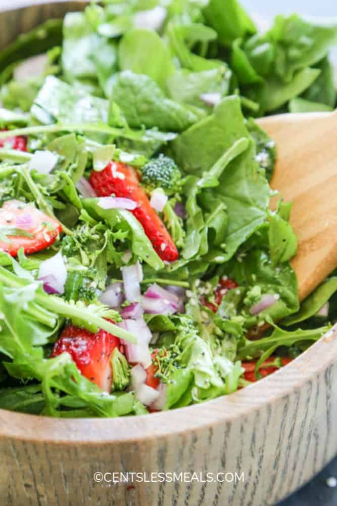 Spinach and strawberry salad in a wooden bowl with a wooden utensil