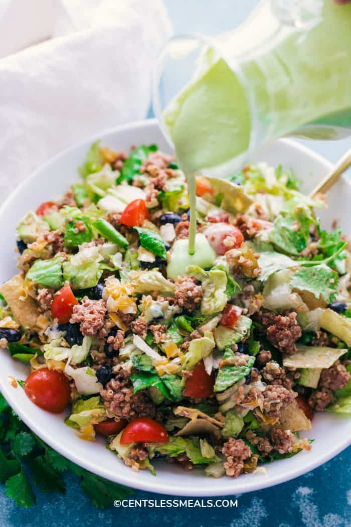 Pouring avocado dressing over a taco salad bowl