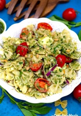 Caprese pasta salad in a white serving bowl with cherry tomatoes and basil beside.
