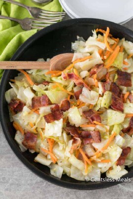 Fried cabbage and bacon in a black pan with a wooden spoon