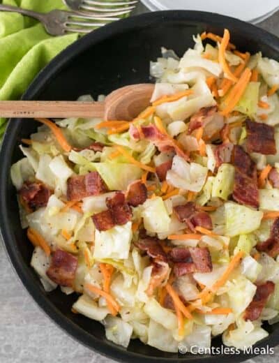 Fried cabbage and bacon in a black pan with a wooden spoon