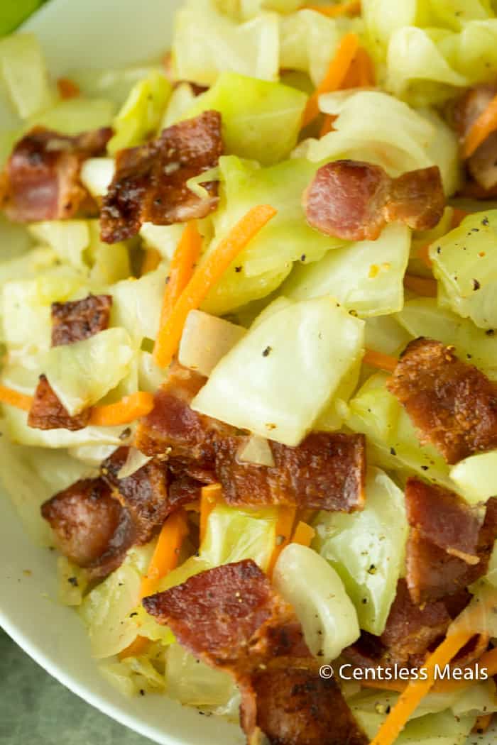 Fried cabbage topped with bacon in a white bowl