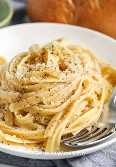 Cacio e Pepe on a white plate with a bun in the background