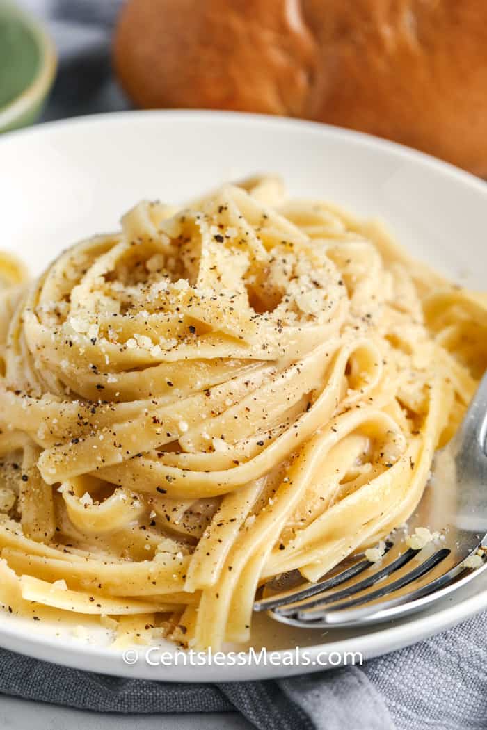 Cacio e Pepe on a white plate with a bun in the background