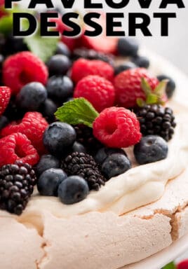 Pavlova topped with berries on a white plate with berries garnished with mint leaves with a title.