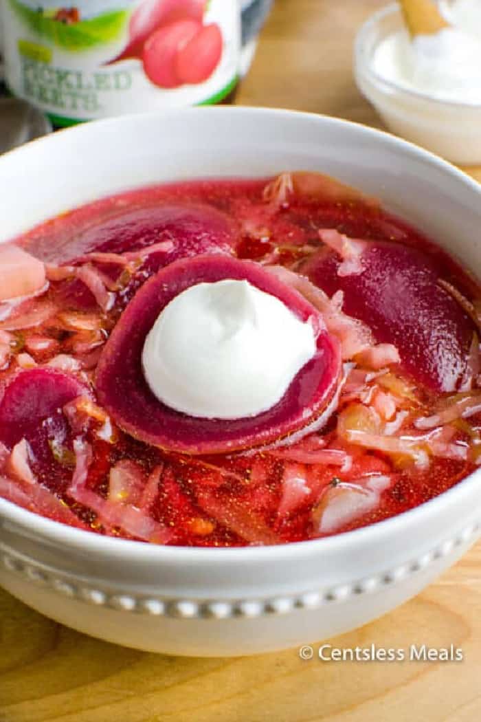 Beet Borscht with a spoonful of sour cream resting on top a sliced beet.