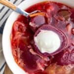 Beet Borscht served in a white bowl with a dollop of sour cream on the top.