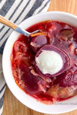 Beet Borscht served in a white bowl with a dollop of sour cream on the top.