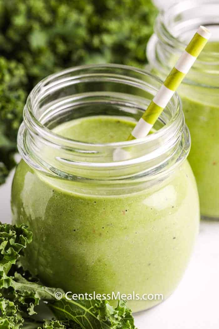 healthy Green Smoothie in a glass with greens in the background