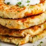 close up of Loaded Mashed Potato Pancakes stacked on a white plate with garnish and dip on top