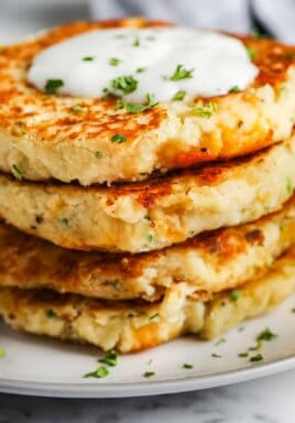 close up of Loaded Mashed Potato Pancakes stacked on a white plate with garnish and dip on top