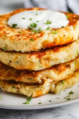 close up of Loaded Mashed Potato Pancakes stacked on a white plate with garnish and dip on top