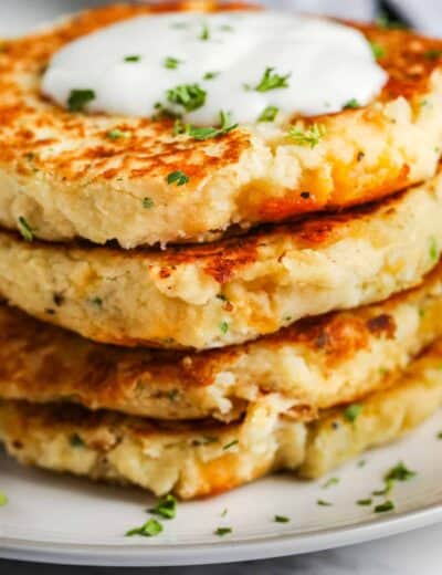 close up of Loaded Mashed Potato Pancakes stacked on a white plate with garnish and dip on top