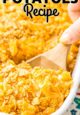 Funeral potatoes in a white casserole dish with a wooden spoon and writing