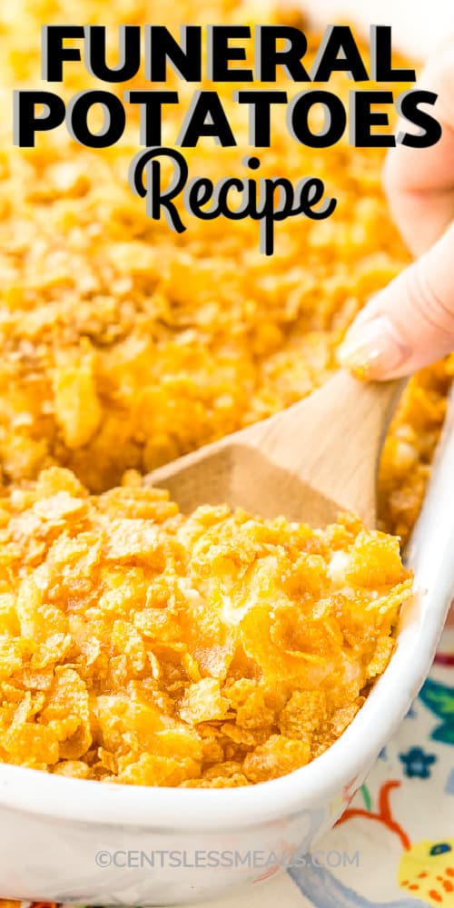 Funeral potatoes in a white casserole dish with a wooden spoon and writing