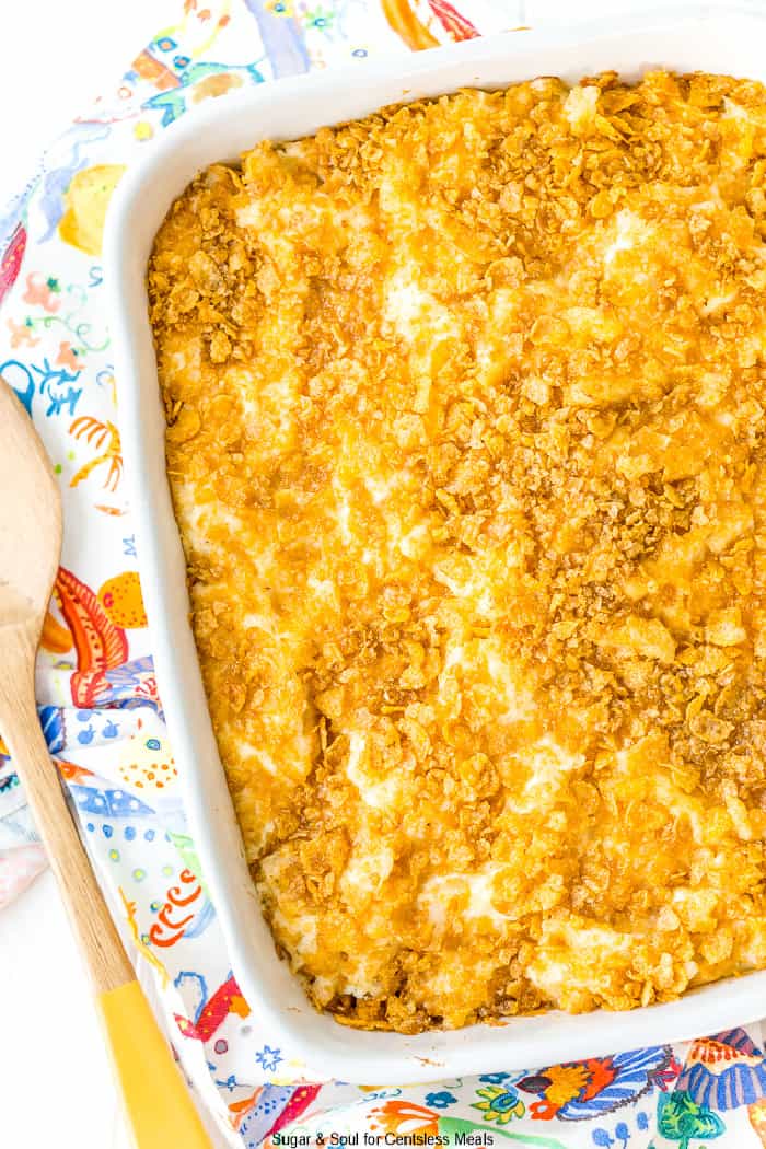 Funeral potatoes in a white casserole dish with a wooden spoon on the side
