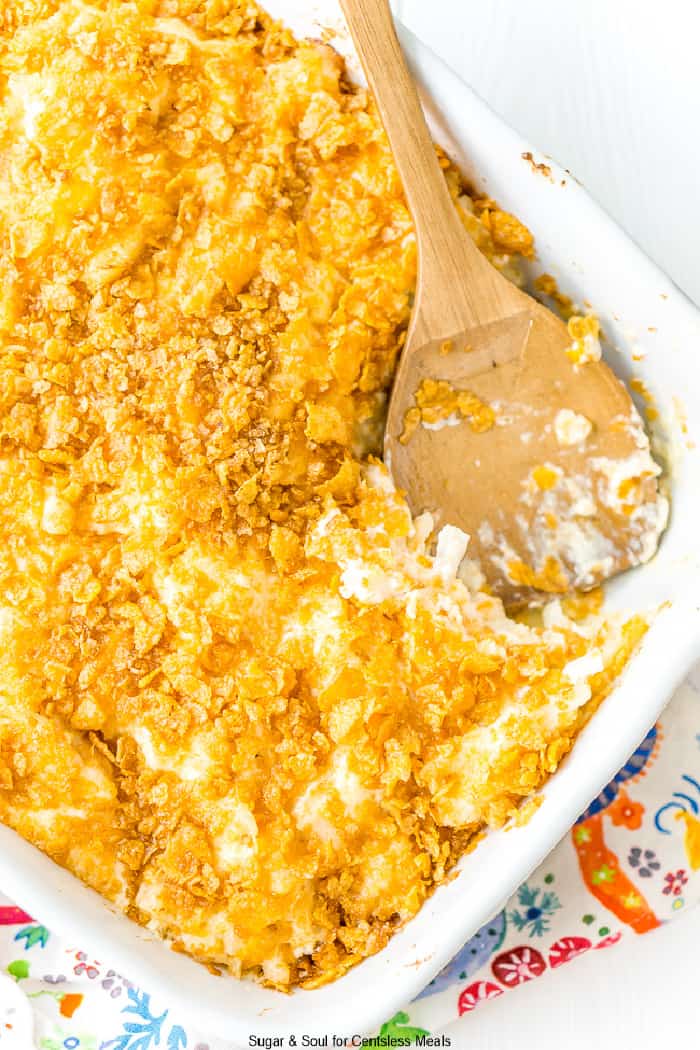 Funeral potatoes in a casserole dish with a wooden spoon