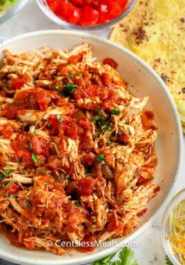 salsa chicken shredded in a bowl with ingredients around the bowl to make Crock Pot Chicken Tacos