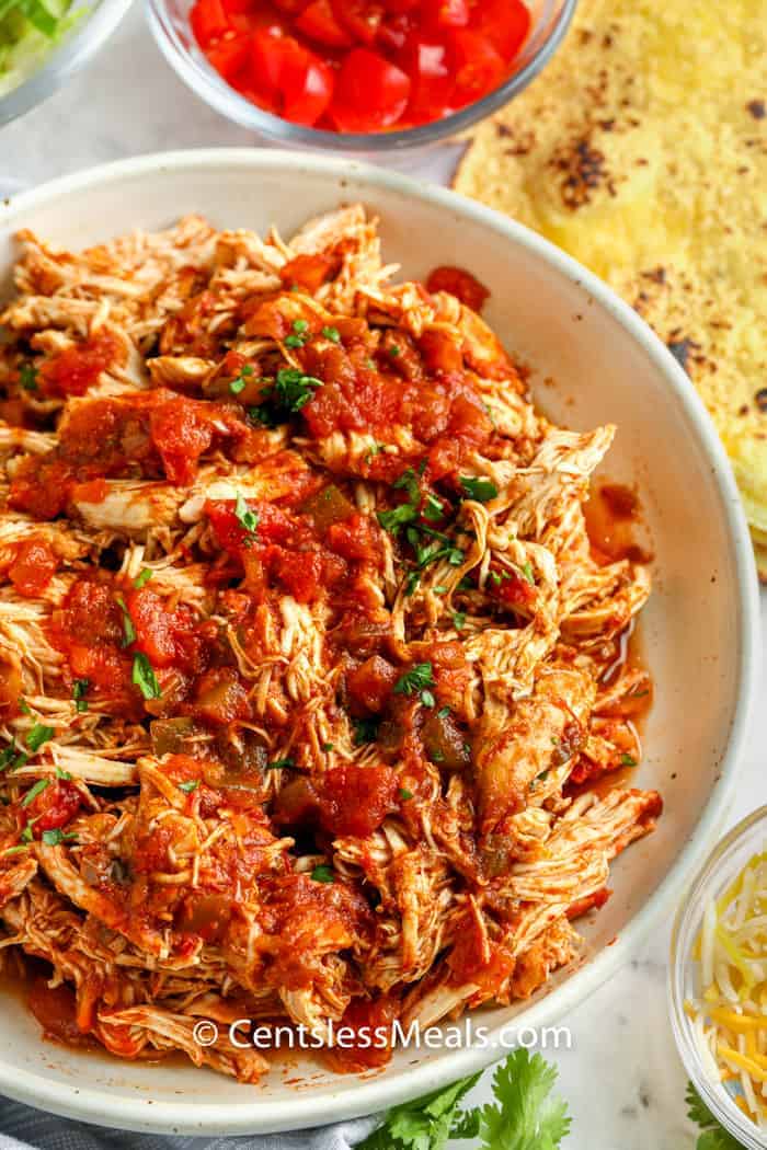 salsa chicken shredded in a bowl with ingredients around the bowl to make Crock Pot Chicken Tacos