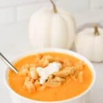 Creamy Butternut Squash Soup in a bowl with decorative pumpkins in the back