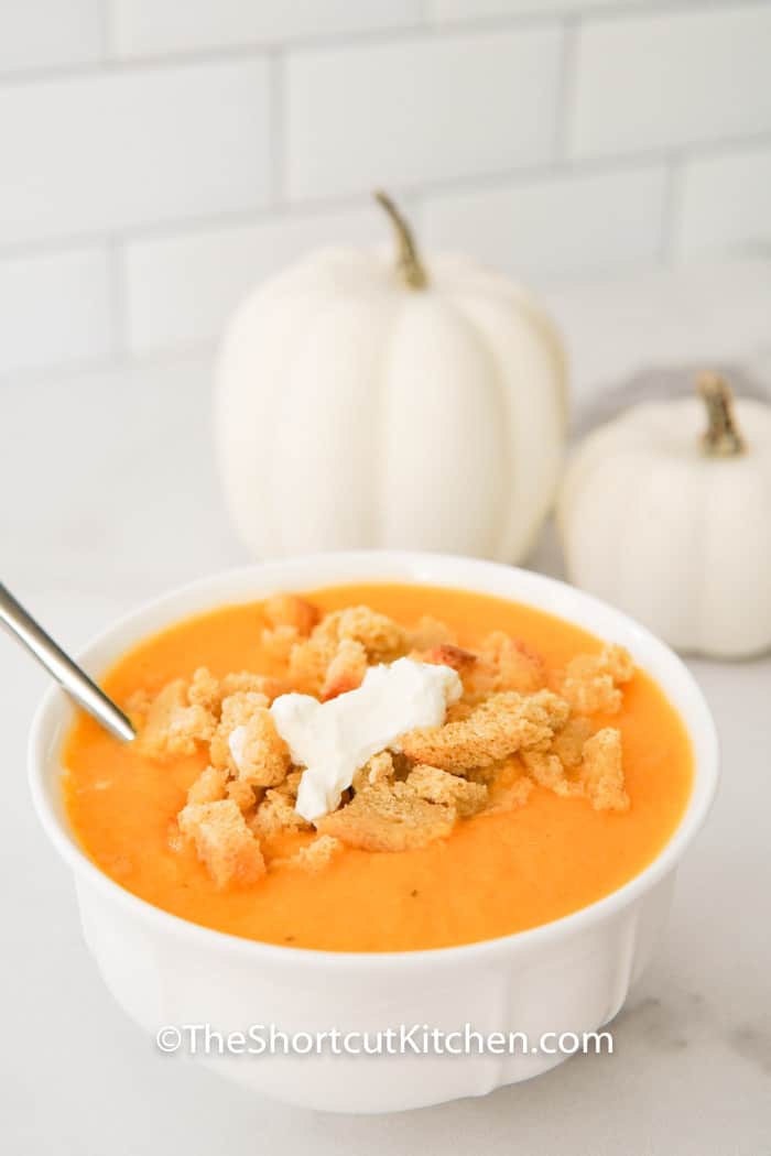 Creamy Butternut Squash Soup in a bowl with decorative pumpkins in the back