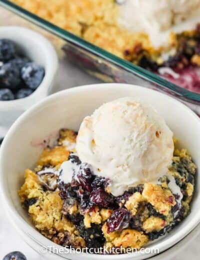 Lemon Blueberry Dump Cake in a bowl with casserole dish full in the back