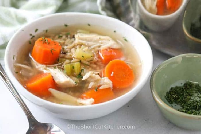 a white bowl full of chicken rice soup with chunks of carrot, celery and chicken.
