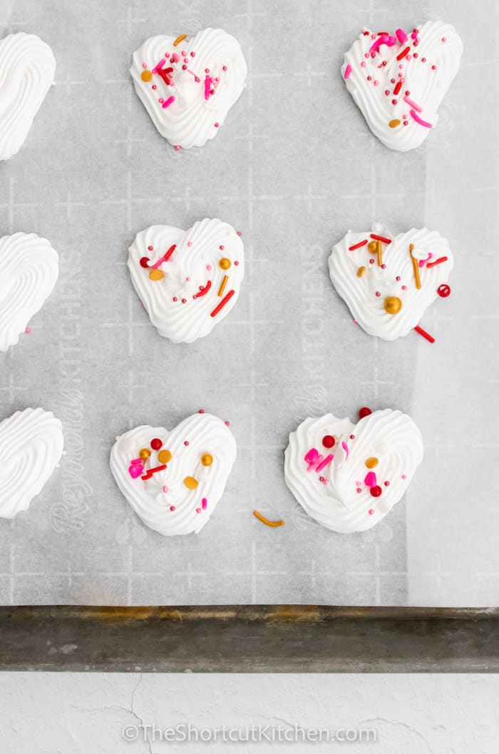 Heart Meringues on a baking sheet with some sprinkles
