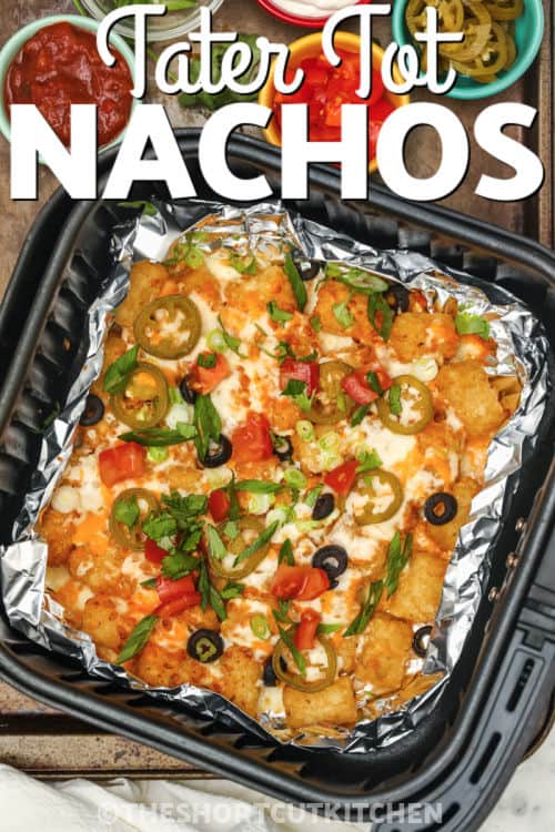 Air Fryer Nachos in a foil lined air fryer basket with toppings assembled on the side, with a title.