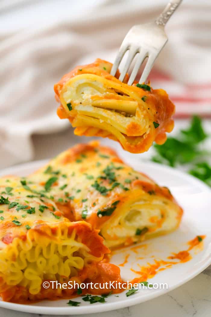 piece of 3 Cheese Lasagna Roll Ups Recipe on a fork with plated dish in the back