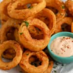 Air Fryer Frozen Onion Rings piled on a plate with dipping sauce on the side.