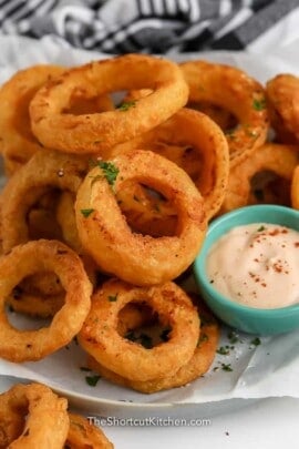 Air Fryer Frozen Onion Rings piled on a plate with dipping sauce on the side.