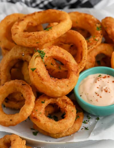 Air Fryer Frozen Onion Rings piled on a plate with dipping sauce on the side.