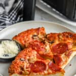 Pizza reheated in an Air Fryer, on a white plate with parmesan cheese on the side