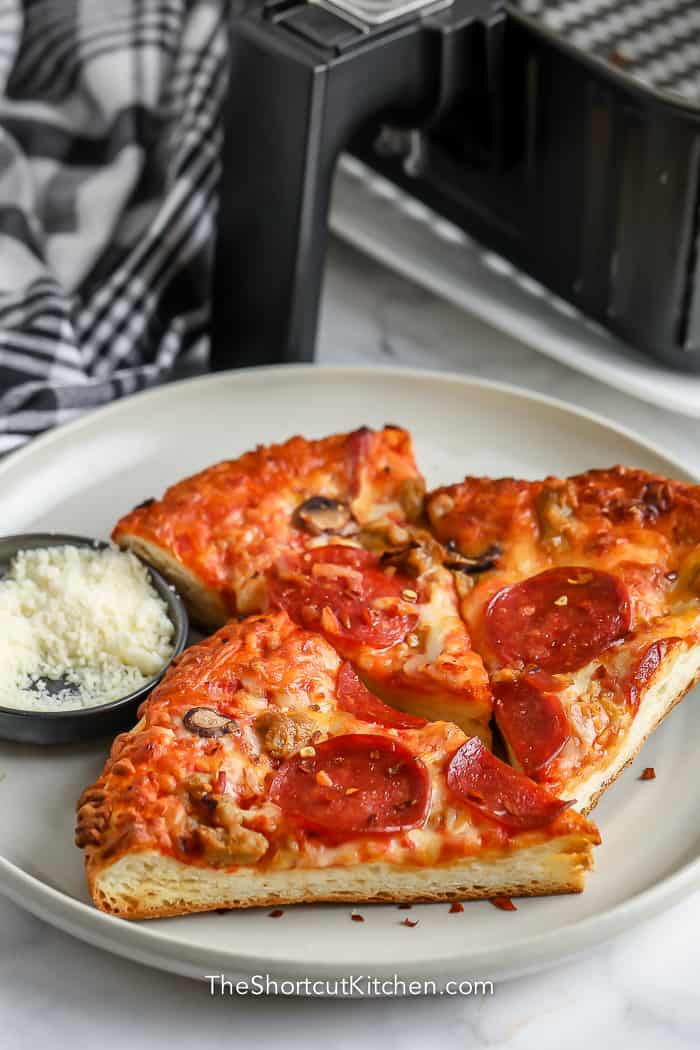 Pizza reheated in an Air Fryer, on a white plate with parmesan cheese on the side