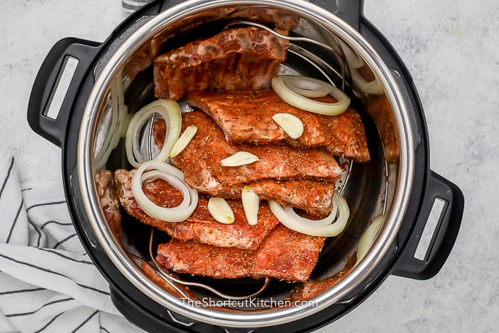Ribs in an instant pot with onion and garlic on top