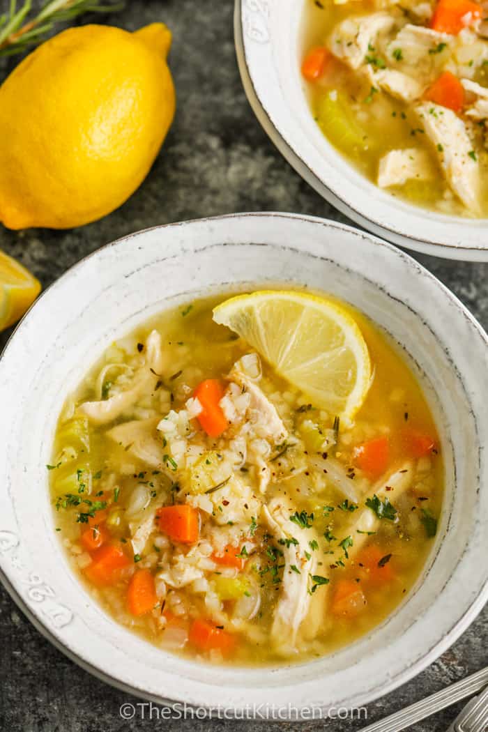 close up of Lemon Chicken Soup in a bowl with lemons beside it