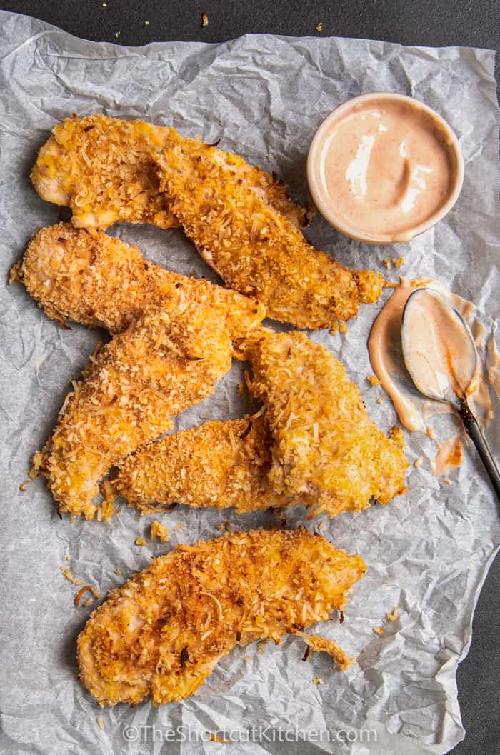 Crispy Coconut Chicken Strips on parchment paper with dipping sauce