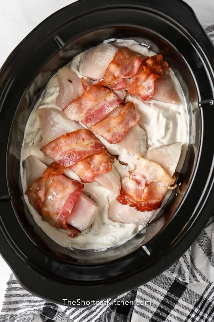 bacon wrapped chicken on a bed of sour cream and mushroom soup in crock pot