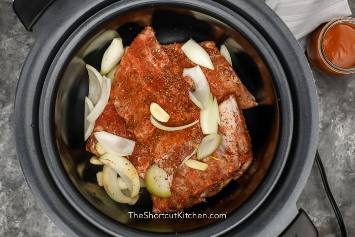 uncooked ribs and onions in a crock pot