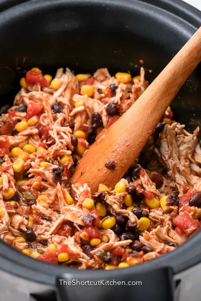 wooden spoon mixing shredded chicken with other ingredients in Crockpot