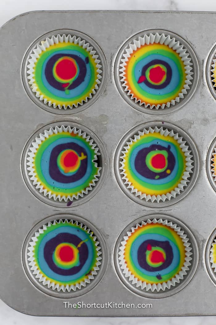 rainbow coloured batter in a muffin pan