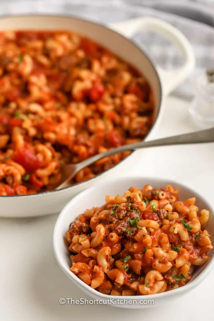 American Goulash served in a white bowl, with a white pan in the background,